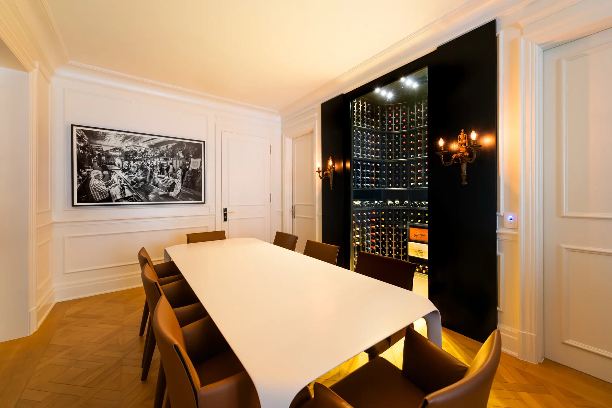 Vista em ângulo da sala de jantar com mesa branca, fotografia na parede e a Adega Frederic Chopin à direita, com garrafas em expositores curvos.